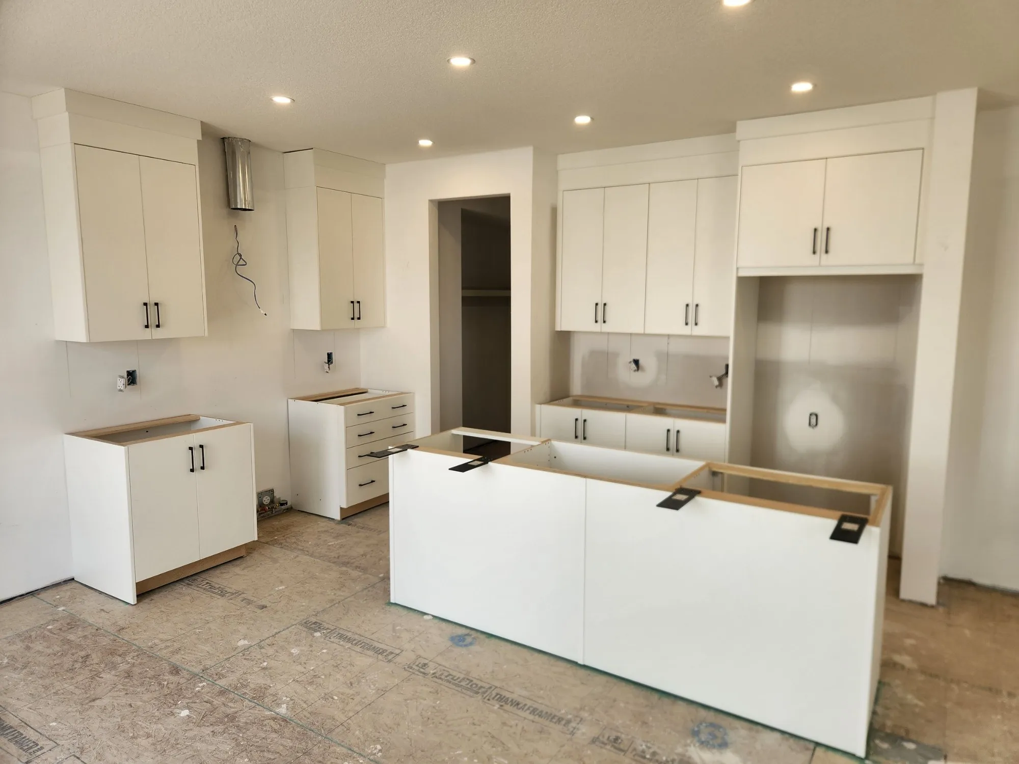 New-build kitchen with white slab doors, black bar pulls, an island and uppers run to the ceiling, installed and ready for countertops