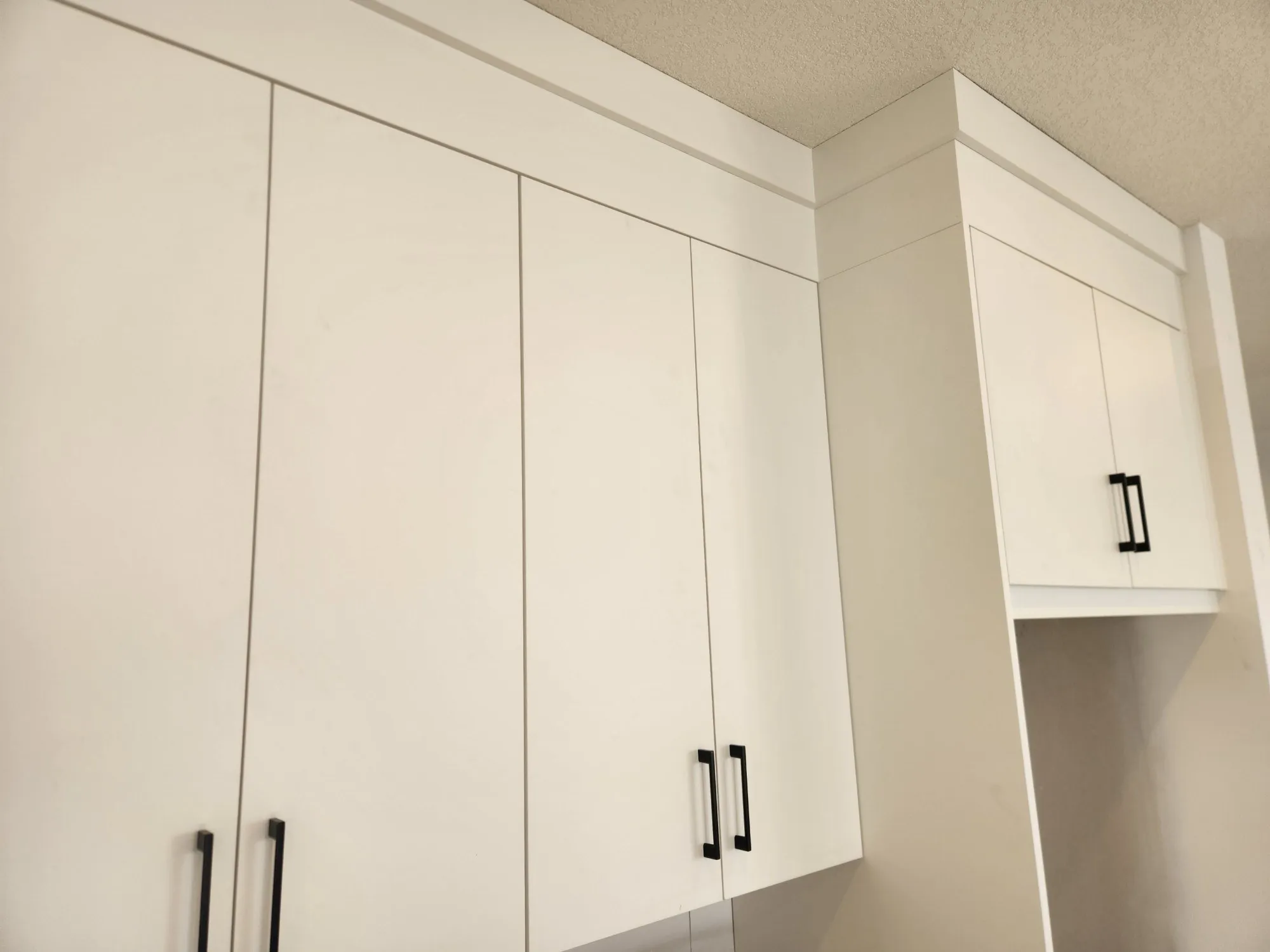 Close-up of white uppers run to the ceiling with risers and crown, tight reveals between doors