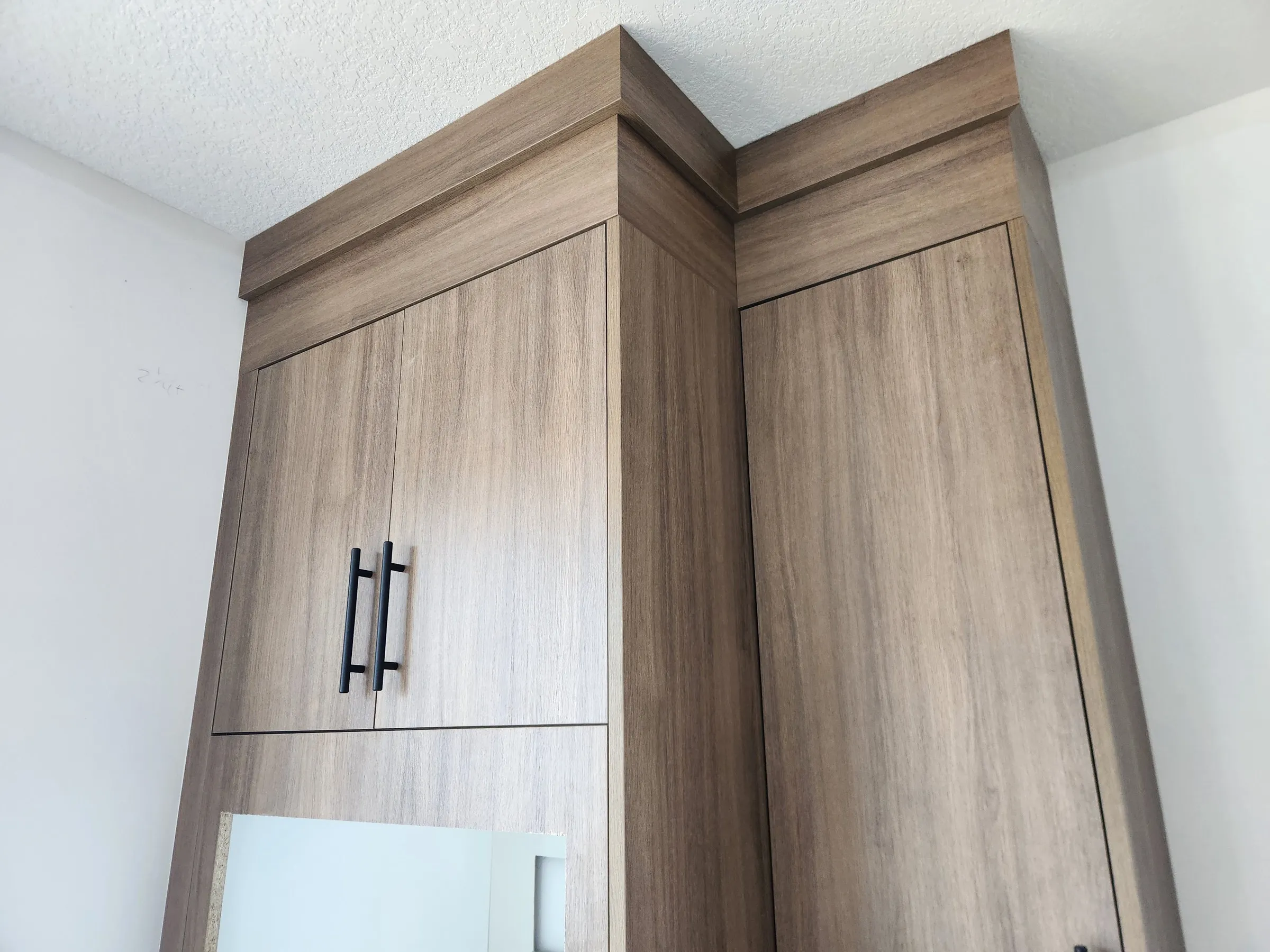Crown moulding wrapped around the corner of two tall woodgrain cabinets, tight to the ceiling